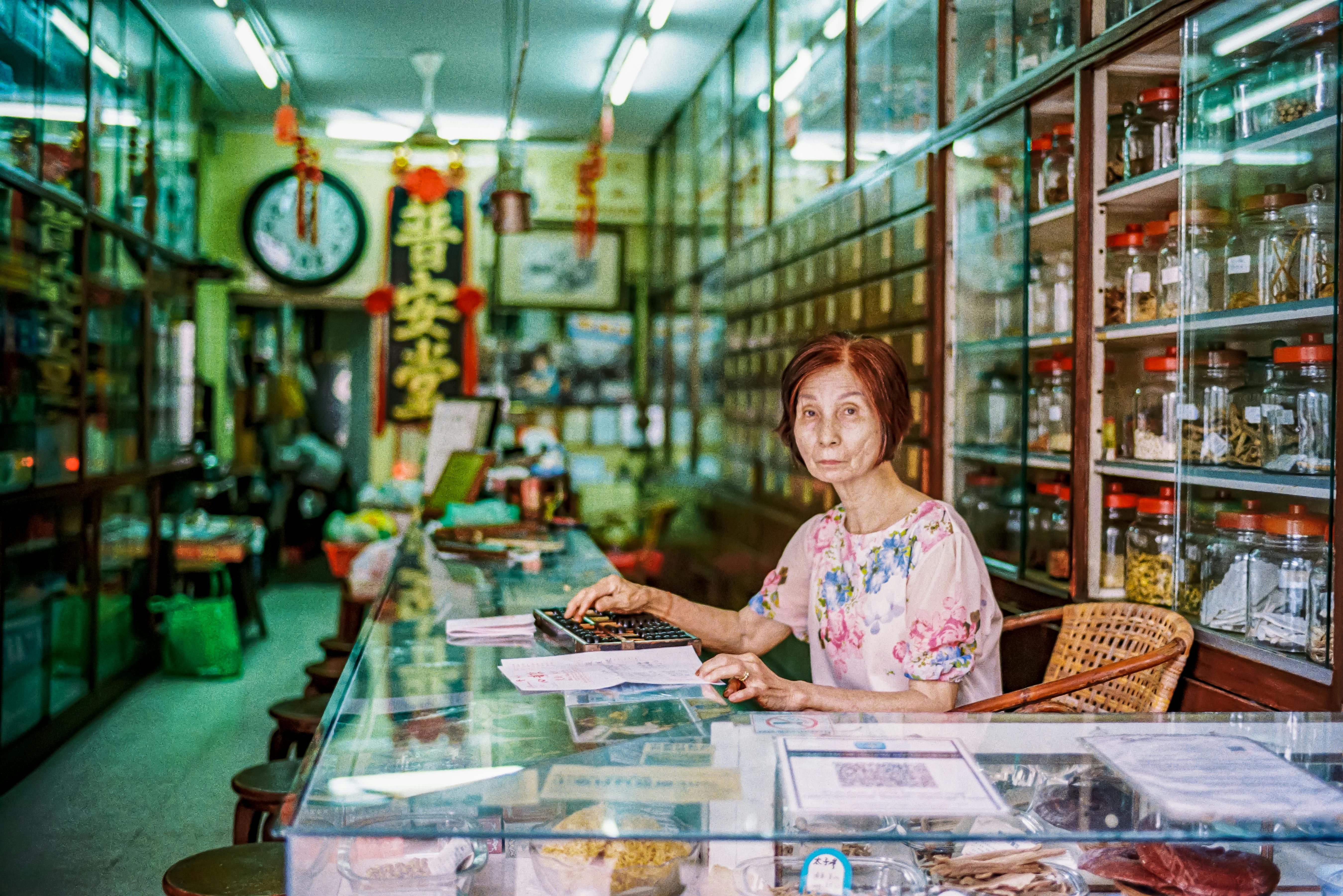 An elderly woman working in a traditional herbal medicine shop in George Town, Penang.