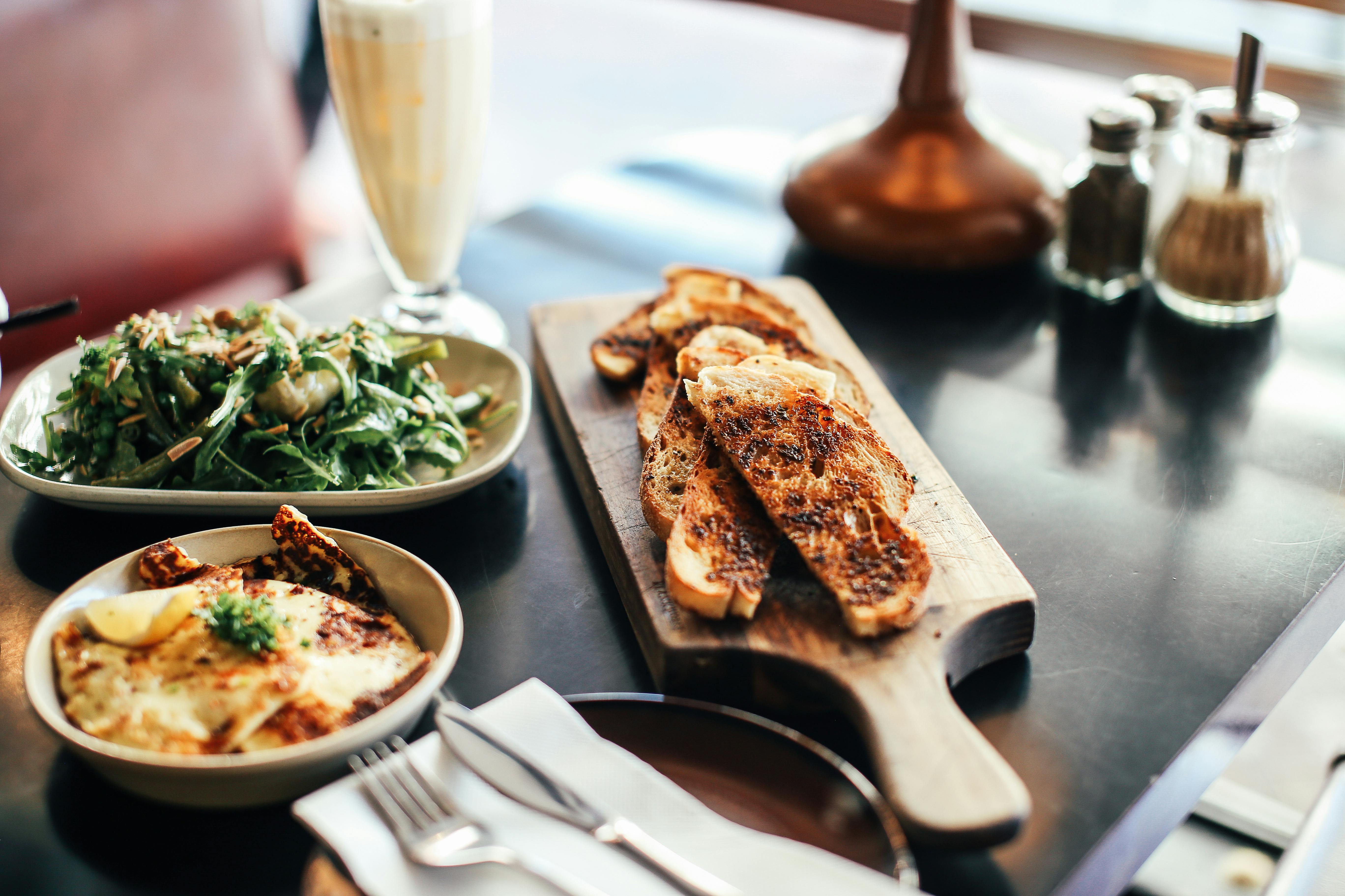 A delicious breakfast setup with toast, salad, and a smoothie on a wooden cutting board, perfect for brunch.