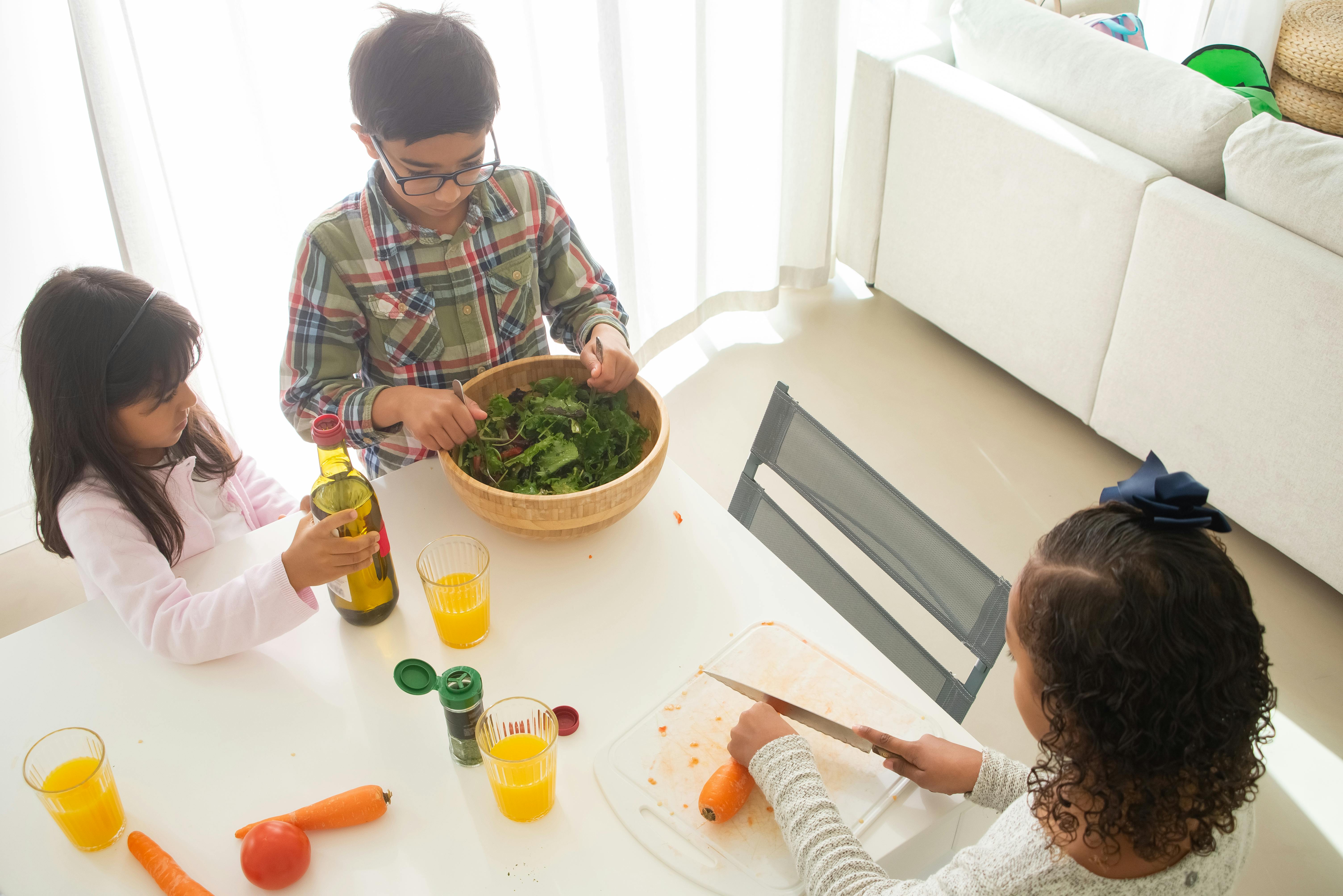 Three children preparing a healthy salad in a bright kitchen setting.