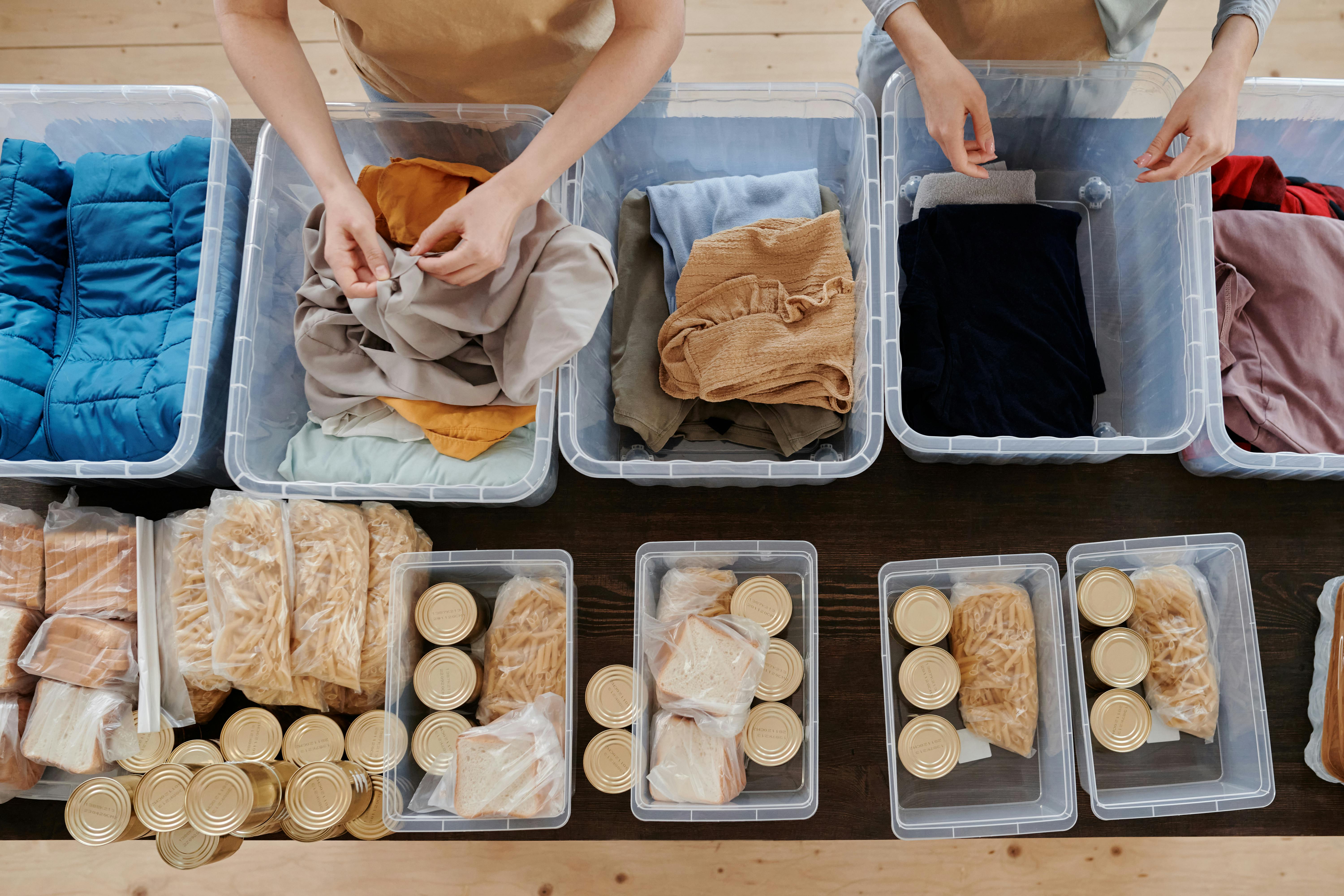 Volunteers organize donated clothes and food cans in clear containers for charity support.