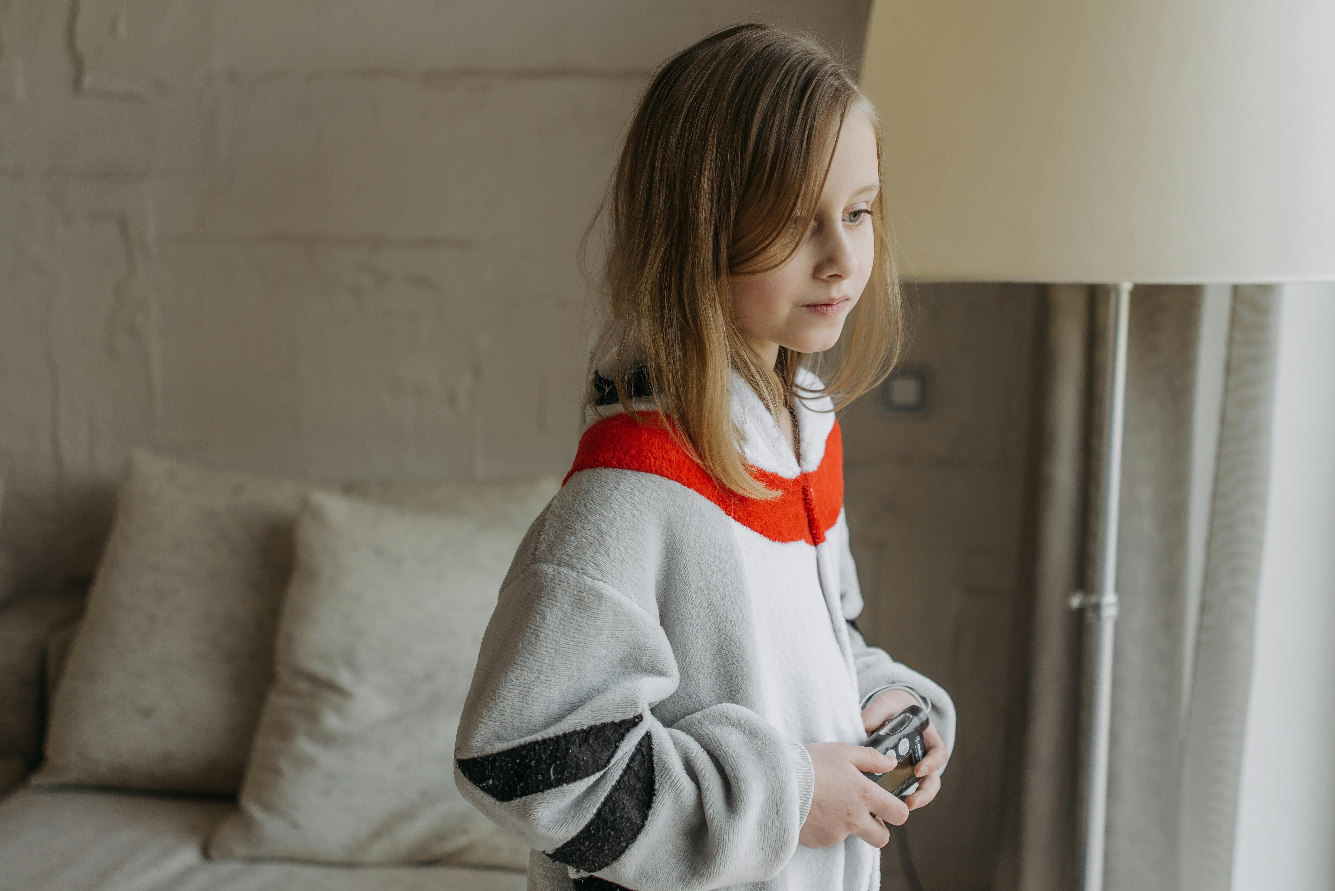 A girl wearing a cozy onesie, holding an insulin pump indoors, symbolizing diabetes awareness.